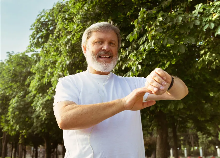 Smiling senior man checking his smartwatch after a walk in the park